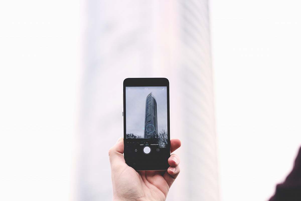 cell phone shallow focus photography of person taking picture of glass tower at smartphone mobile
